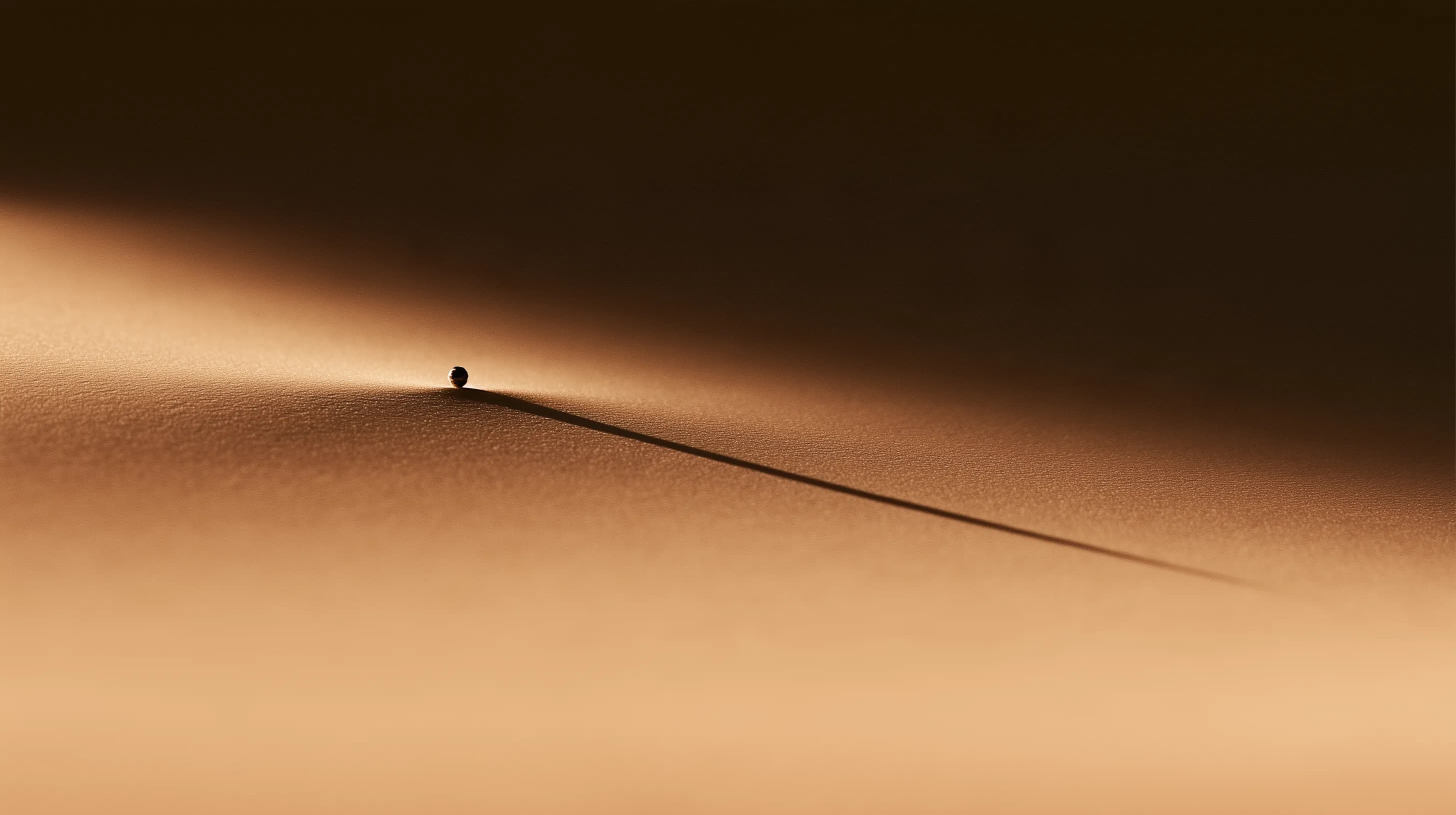 A small sphere resting at the edge of a ridge, casting one long shadow.
